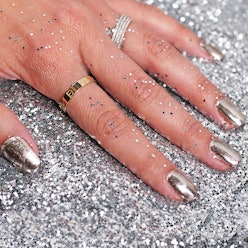 A closeup of a hand with DIY chrome nails, resting on a pile of silver glitter