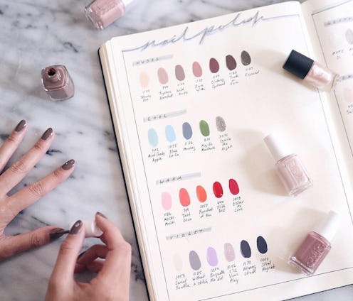 A woman applying nail polish next to a book with various nail polish swatches