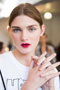 A brunette model with blue eyes, wearing a white shirt and red lipstick, posing with her fingers int...