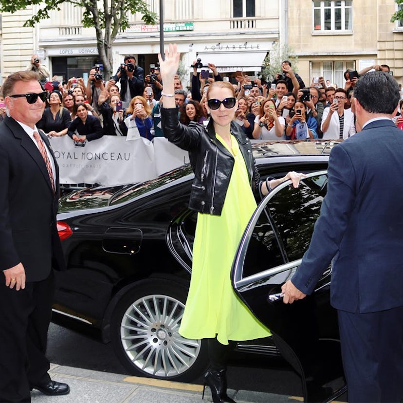 Celine Dion waving to her fans while wearing a yellow dress and a black leather jacket 