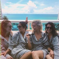Four millennial women in matching grey robes at a bachelorette party