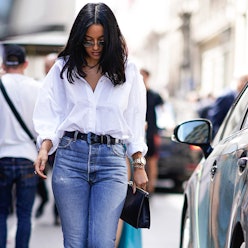 A brunette woman in a white shirt and perfect straight-leg jeans walking down a street