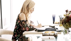 Rachel Zoe in a floral-patterned top, sitting at the table and writing in her planner