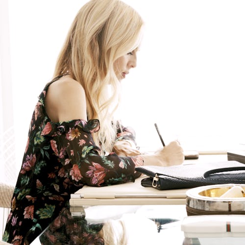 Rachel Zoe in a floral-patterned top, sitting at the table and writing in her planner