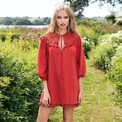 A blonde model wearing a red boho dress while standing in a garden