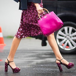A woman walking in a heart-patterned knee-length skirt and matching heels, accessorized with a pink ...