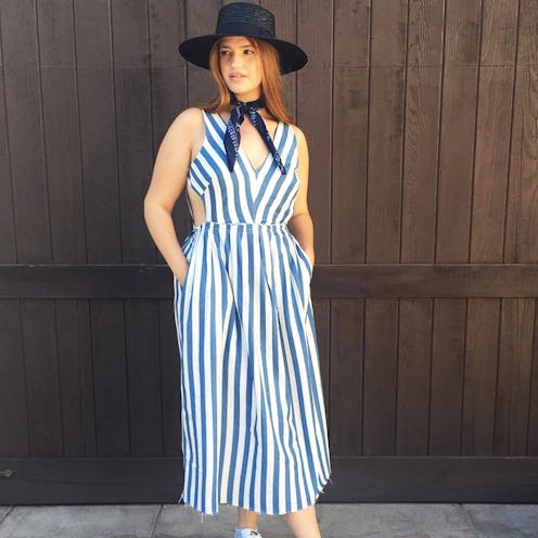 A woman wearing a black hat and neck scarf, and a white-blue striped dress by one of the fashion bra...