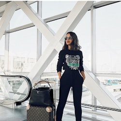 A woman posing at an airport in a shirt with a tiger on it and her luggage next to her