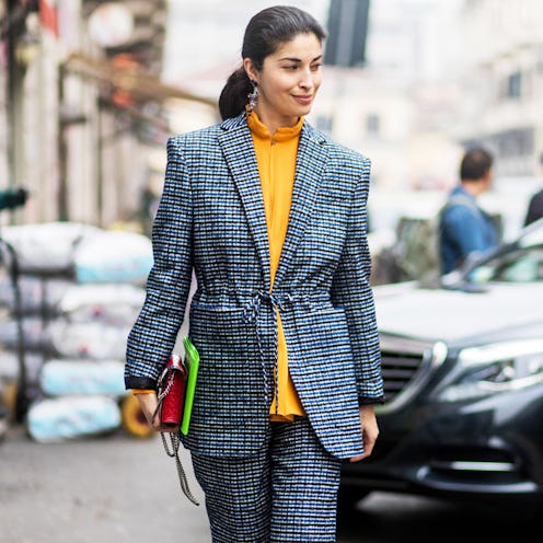 A woman walking down the street in a grey suit with a yellow top