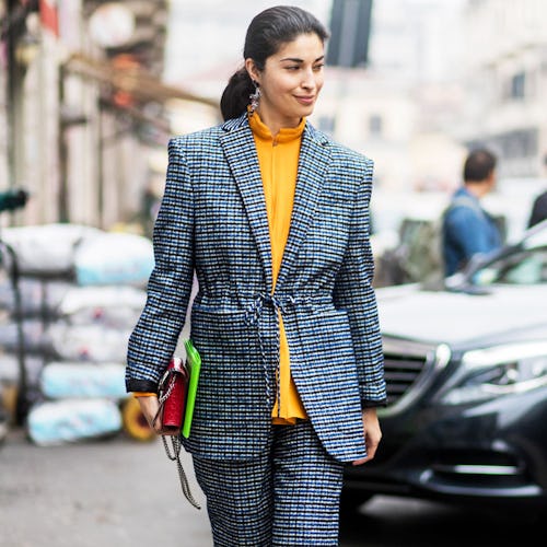 A woman walking down the street in a grey suit with a yellow top 