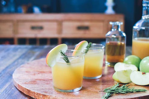 Two glasses with the Rosemary Mezcal Apple Cider, apple slices, rosemary leaves and two bottles