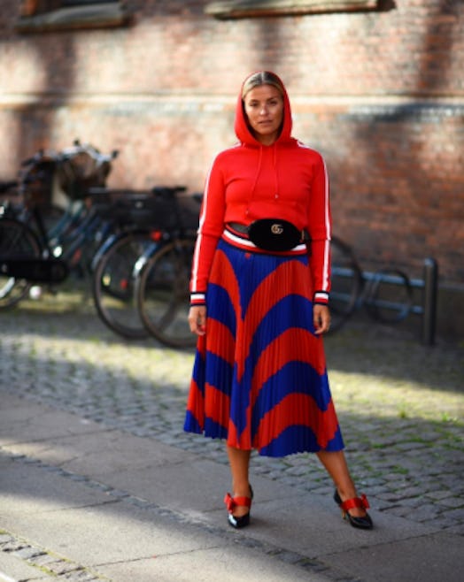 A model posing in a red hoodie and in a blue and red skirt