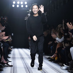 Alexander Wang in a black sweater, trousers, and boots waving while walking on a runway