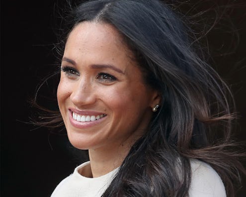 A close-up portrait of Meghan Markle smiling in a white top with wind in her dark hair