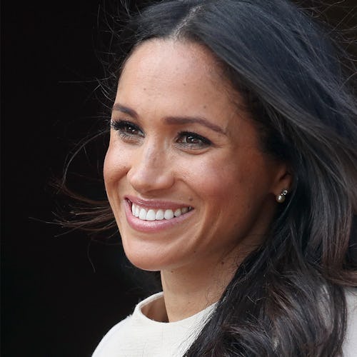 A close-up portrait of Meghan Markle smiling in a white top with wind in her dark hair