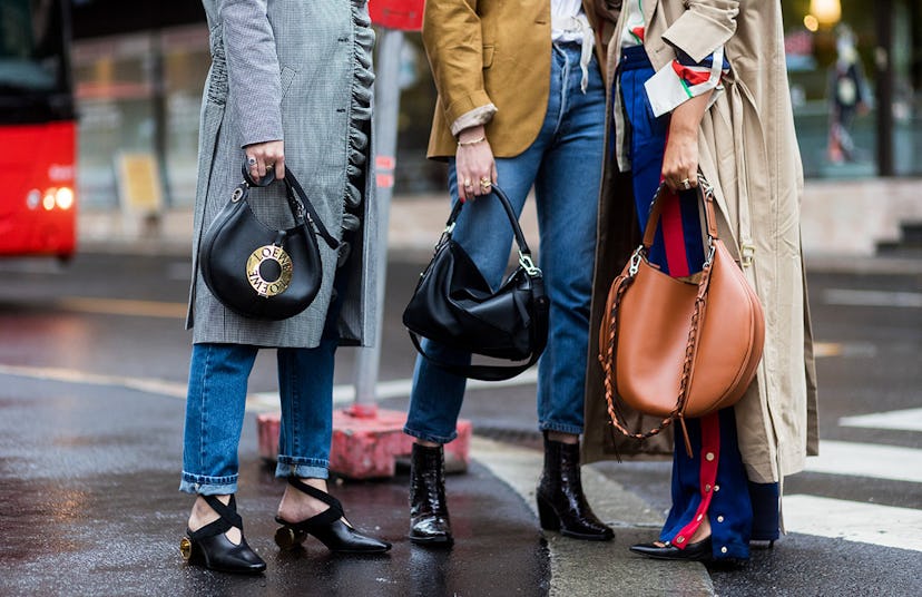 Three models holding handbags on a street