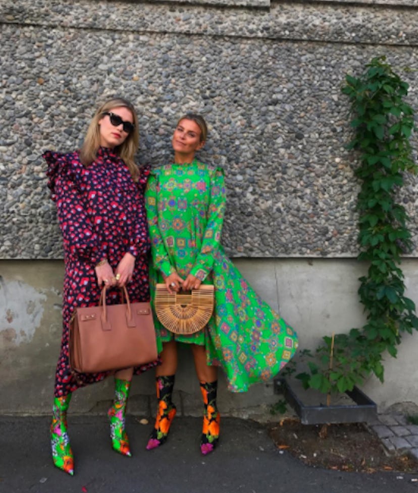 Two girls posing in purple and green dresses while holding brown handbags 