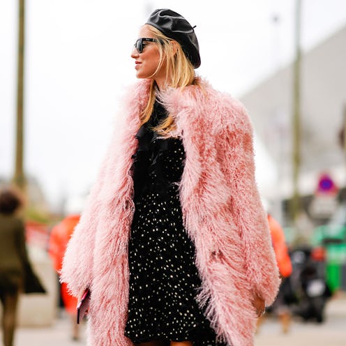 A woman in a black beret, black dress, sunglasses and a pink faux fur coat