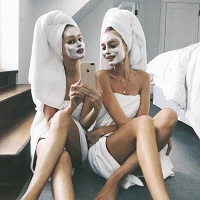 Two girls with white creams over their faces taking a mirror selfie