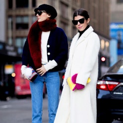 A woman in a black coat, white sweater, burgundy scarf, black hat and denim jeans, and a woman in a ...