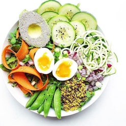 A plate of healthy foods, including avocado, eggs, carrot, couscous, onion, green beans and cucumber