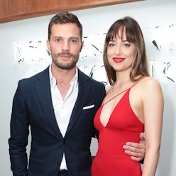 Jamie Dornan in a blue suit next to Dakota Johnson wearing a red dress at a red carpet event