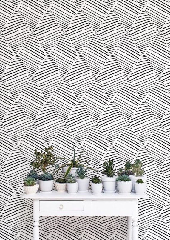 A wall with a removable white-black geometric print removable wallpaper and a white desk with 12 sma...