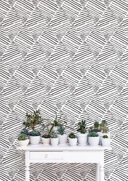 A wall with a removable white-black geometric print removable wallpaper and a white desk with 12 sma...