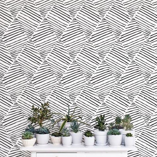 A wall with a removable white-black geometric print removable wallpaper and a white desk with 12 sma...