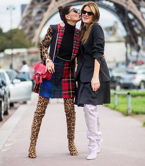A brunette woman in a plaid - leopard-print outfit kissing a woman in a black dress and white boots ...