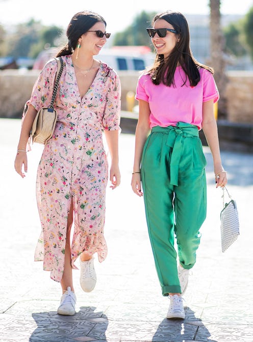 A girl in a maxi dress walking next to her friend in green pants and a pink t-shirt, both wearing Tr...