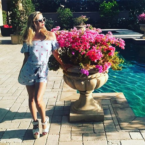 Reese Witherspoon in her home in a blue romper, next to a large potted plant