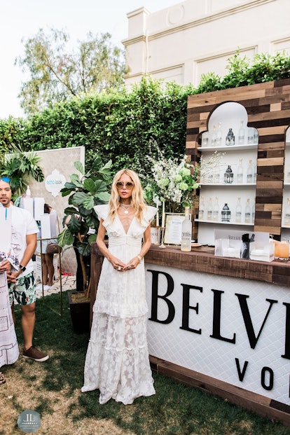 A blonde woman standing next to a Belvedere Vodka promo stand while wearing a white dress