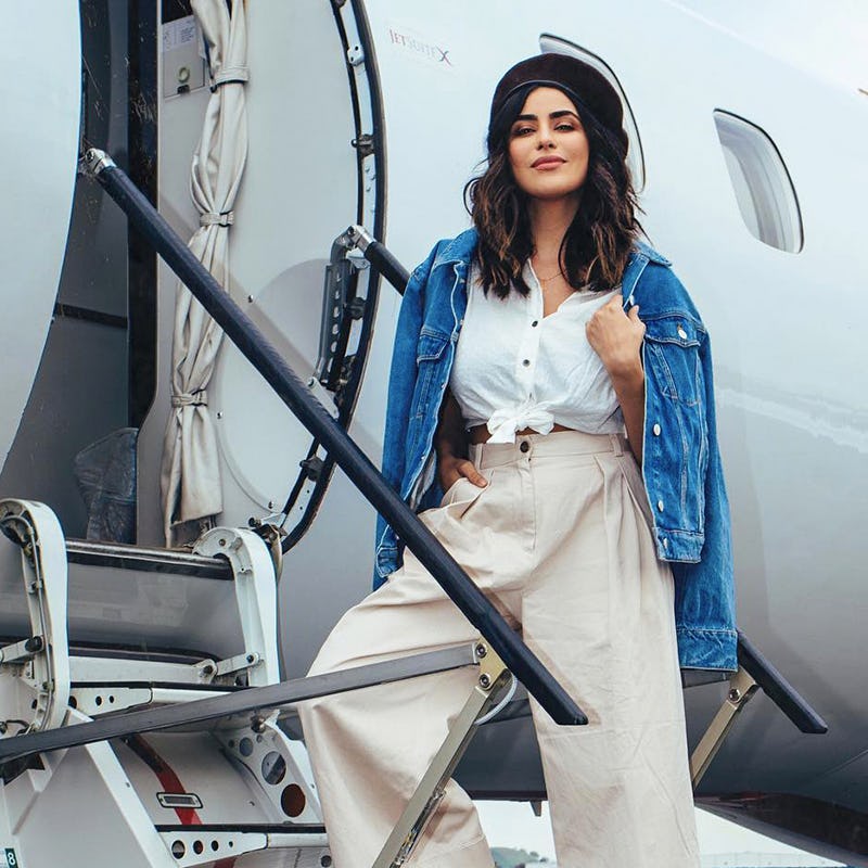 A brunette posing in beige wide-le trousers, white shirt with denim jacket over her shoulders and a ...