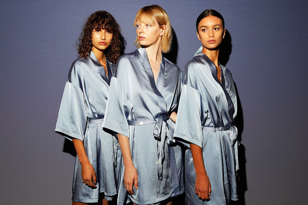 Three women in blue silk capes posing with clear skin without acne issues