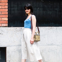 A model with short black hair, sunglasses, a blue top and white skirt 