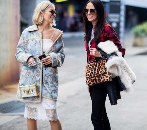 Two women on the street, one in a blue jacket and white bag and the other in a plaid jacket and leop...