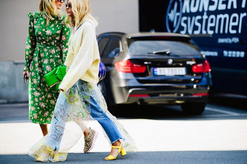Two women walking at a parking lot, one in a hoodie with jeans and heels and the other in a green dr...