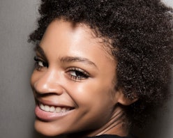 A model with curly brown hair smiling at the camera after applying a face oil