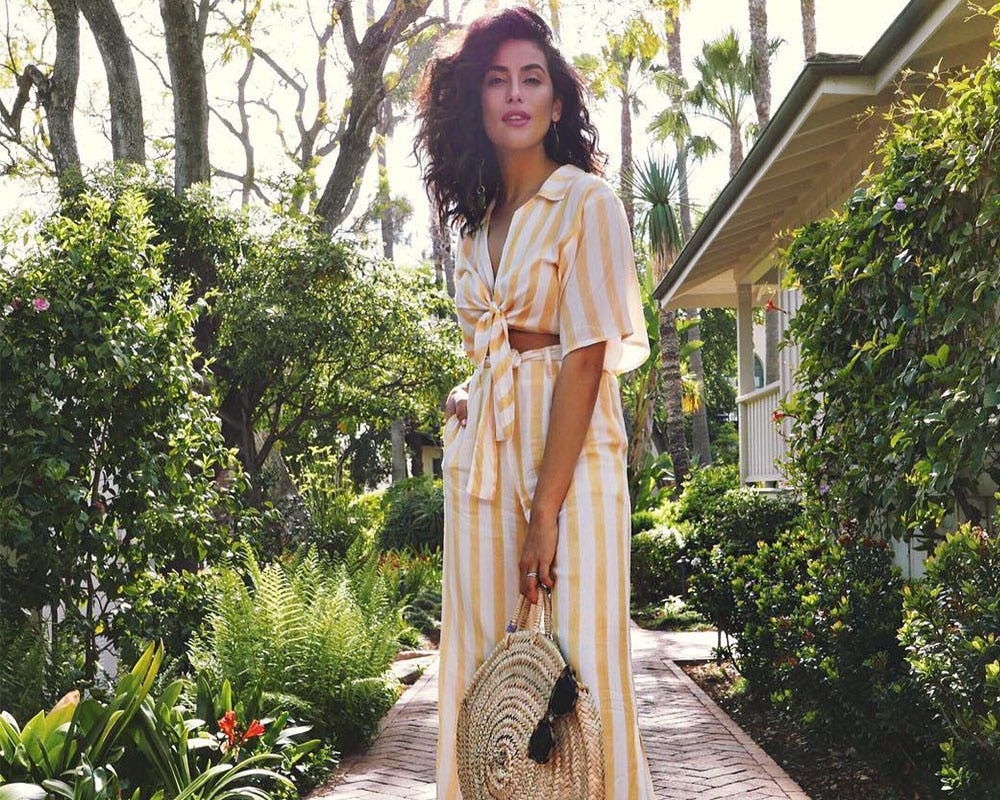 A model in a striped tied-up blouse, matching pants and a woven bag 