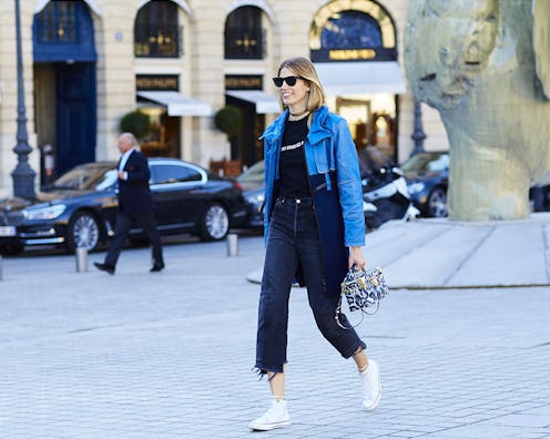 A woman in a black shirt and pants, blue crop jackets, and white high-top sneakers