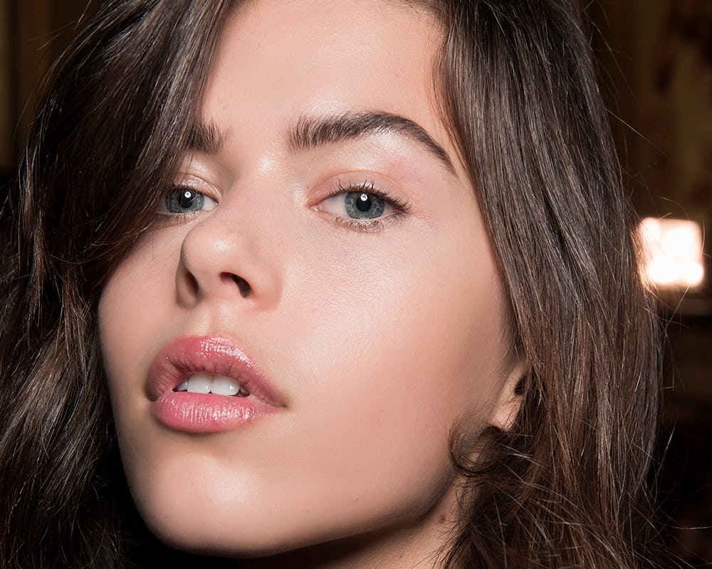 A woman with long brown hair posing, pursing her lips and showing her no lipstick look