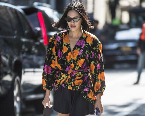 A woman with a bob haircut, wearing a floral top and black shorts while walking the street