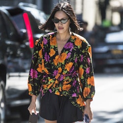 A woman with a bob haircut, wearing a floral top and black shorts while walking the street