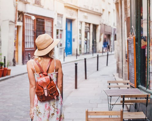 The back of a woman in a floral dress, straw hat and a small brown leather backpack on vacation
