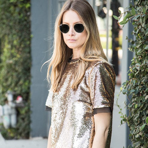A blonde woman with sunglasses wearing a sequin shirt during the day