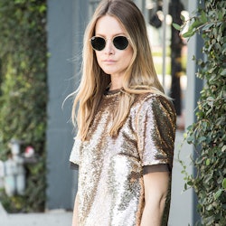 A blonde woman with sunglasses wearing a sequin shirt during the day