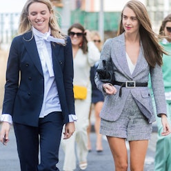 Two women wearing chic outfits walk down the street while talking and smiling
