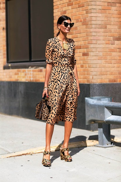 A woman in a leopard print dress and matching sandals, with tied-up hair and heart-shaped sunglasses...