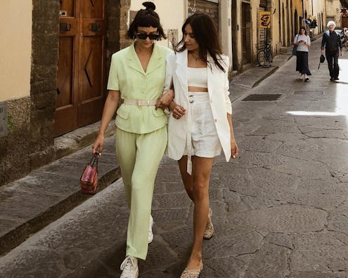 Two women strolling down the street hand in hand wearing matching summer sets in lemon-green and whi...